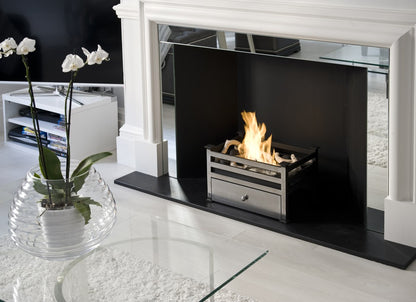 CHELSEA Polished Steel Bioethanol Grate in fireplace opening with white surroundings and flowers