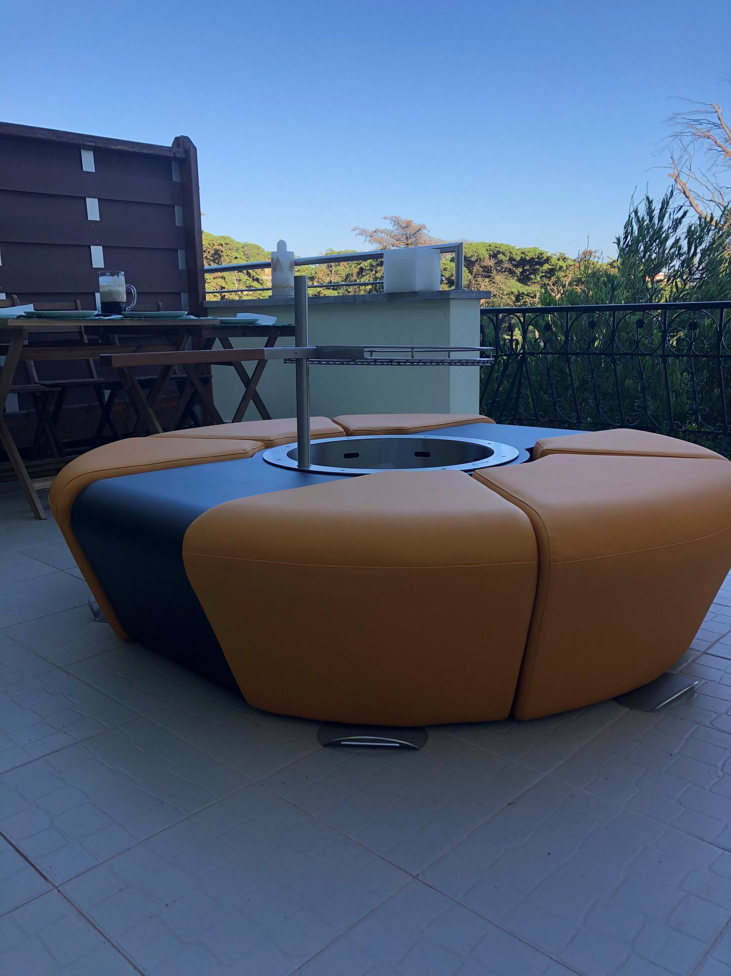 Circus with wood burner barbecue grill and saffron yellow ottomans. Picture on a terrace.