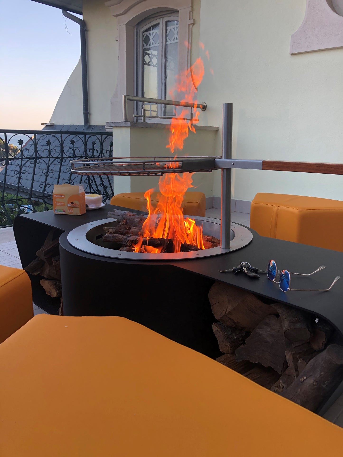 Circus with wood burner barbecue grill and saffron yellow ottomans. Close up on grill and flame. Picture on a terrace.