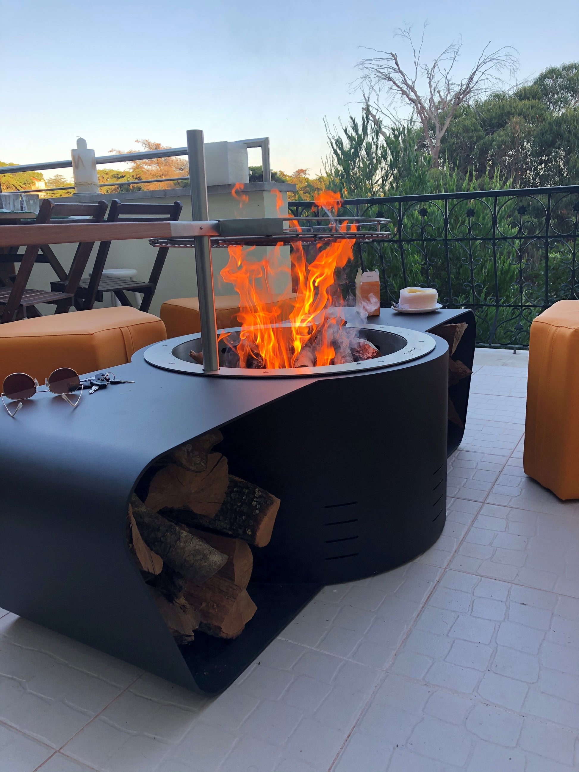 Circus with wood burner barbecue grill and saffron yellow ottomans. Close up on grill and flame. Side view. Picture on a terrace.