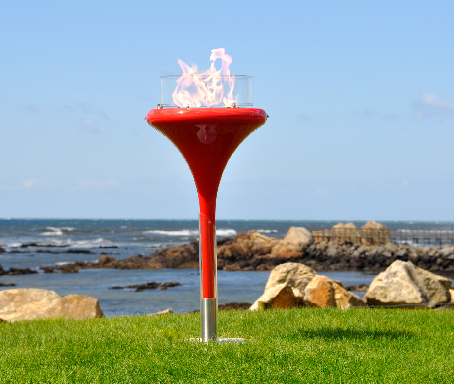 Flut Red fixed on the ground in seaside garden with see and pier in the background.