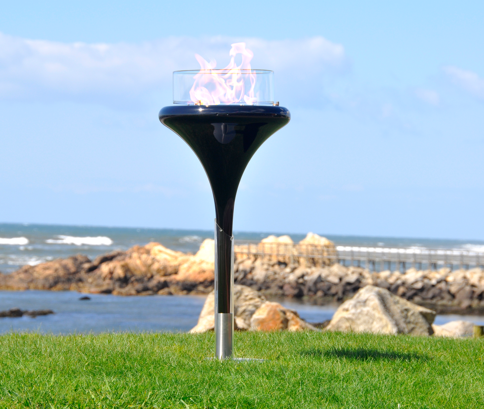 Flut Black fixed on the ground in seaside garden with see and pier in the background.