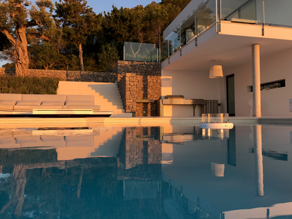 Flut White fireplace set up in outdoor swimming pool. Sitting area and woods in the background.