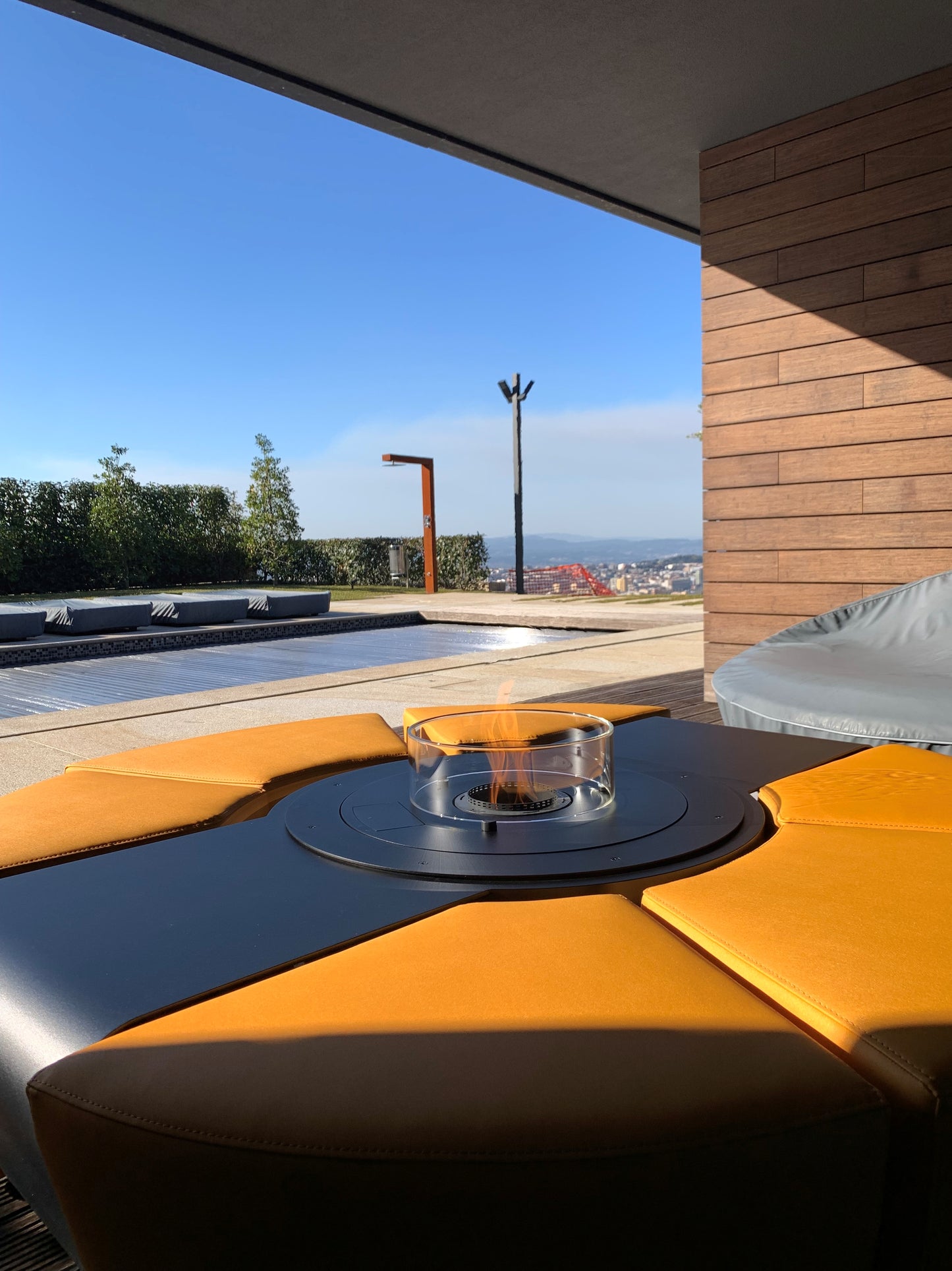 Circus with automated bioethanol burner and saffron yellow ottomans on semi-covered patio with swimming pool.