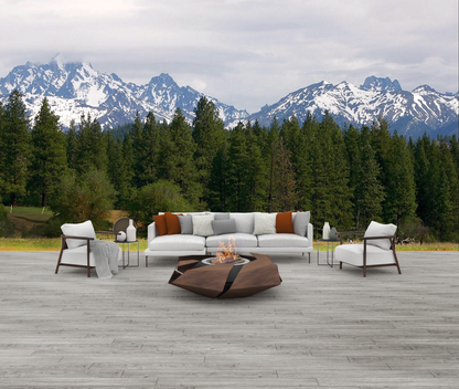 Stravaganza firepit with charcoal burner in rusted corten steel finish in stone-tiled patio with sofa and couches. A beautiful forest and the Alps are in the background.